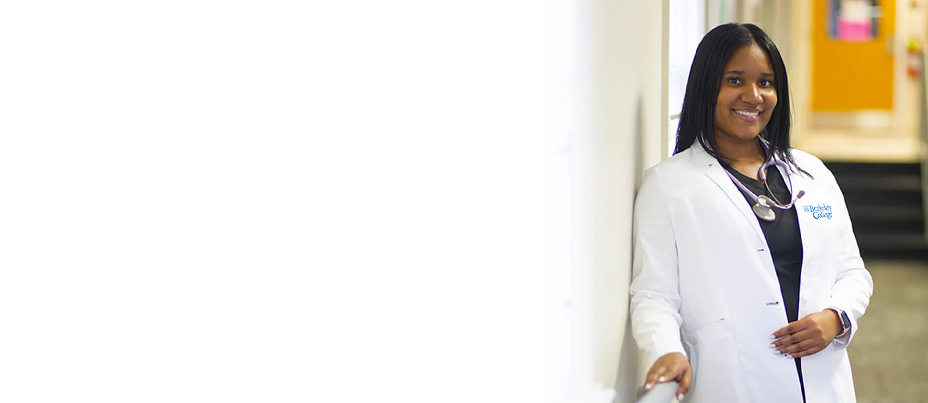 Image: A healthcare professional in a white lab coat stands confidently by a wall, wearing a stethoscope and displaying professionalism.