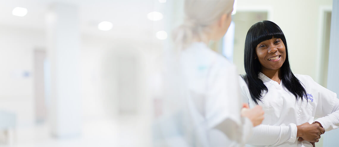 A woman wearing a white lab coat is positioned in a hallway, symbolizing her role in a scientific or medical environment